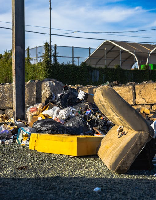 A collection of rubbish and waste materials scattered on a gravel surface in an outdoor setting. The pile includes several black plastic rubbish bags, some torn open revealing assorted waste, along wi